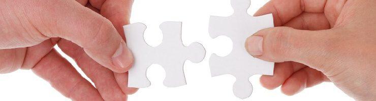 two hands each holding a white puzzle piece on white background