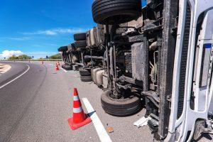 Overturned 18-wheeler cargo truck on the road with hazard cones