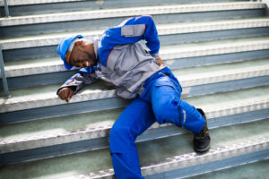 a man in working gear lays injured at the bottom of a flight of stairs.