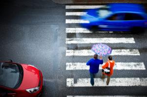 pedestrian crosses street while car drives through crosswalk