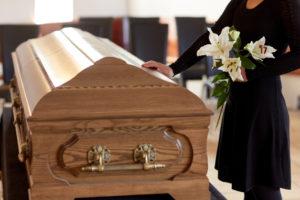 A woman holding flowers lays her hand on the coffin of a family member.