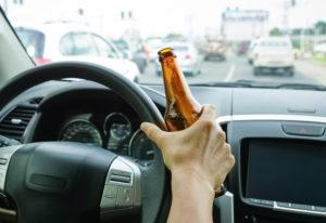 man holds alcoholic beverage while driving