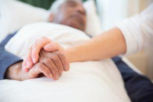 Nursing home resident in bed with someone holding his hand