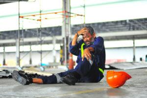 A worker holds his head and knee after an injury on the job.