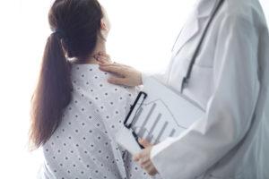 Female patient in a robe with a doctor feeling her neck as she suffers from pain.