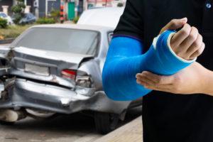 A person in a cast stands by their crashed car.