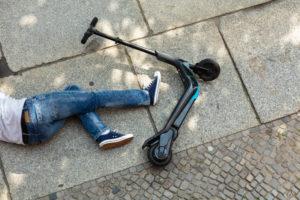 Driver's legs on the ground next to their scooter after an accident