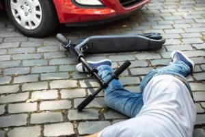 man lying in front of red car after scooter accident