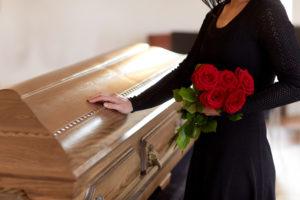 Woman standing next to a casket with her hand on top and holding flowers