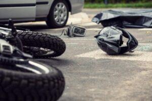 Motorcycle on its side with scattered belongings and car responsible for wreck in background.