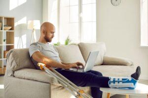 Gentleman with a broken leg working on his couch with a laptop on his lap.